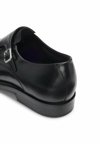 Schwarzer Lederschuh mit abgerundeter Spitze, einzelnen Schnallendetail und strukturiertem Innenfutter. Verfügt über eine niedrige, strapazierfähige Sohle mit horizontalen Linien.