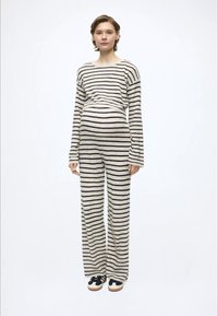 Csíkos kényelmes szett puha anyagból; hosszú ujjú, laza szabású, széles szárú nadrág krém és fekete csíkokkal, sportcipővel párosítva.