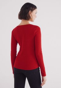 Rode lange mouwen top met een geribbelde textuur en een brede halslijn, fitted in de taille, gecombineerd met donkere jeans. Glad stofafwerking.
