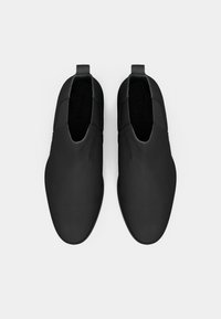Paire de chaussures à enfiler noires avec des bouts ronds et des languettes au talon, présentées vues de dessus sur un fond clair.