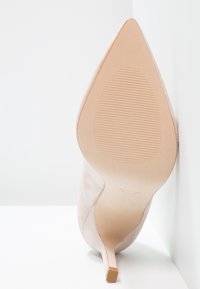 Nude mockask stilettohæl med spetsig tå, med en slät sula och grepp linjer, designad för elegant stil och stabilitet.