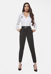 Biała koszula z guzikami z haftowanym wzorem, czarne spodnie o wysokim stanie z gładkim pasem i czarne szpilki z ostro zakończonym noskiem.