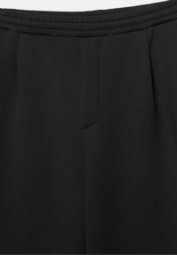 Pantalon à taille élastique noire avec plis avant et braguette cachée, présenté en gros plan sur la partie supérieure avant.