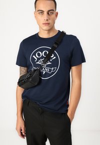 T-shirt bleu marine avec un design graphique blanc et le texte "JOOP!". Associé à un pantalon noir et un petit sac bandoulière noir avec des détails en chaîne.