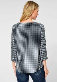 Top a fantasia houndstooth blu navy e bianco con scollatura ampia, maniche a tre quarti e orlo curvo. Texture morbida e vestibilità rilassata.