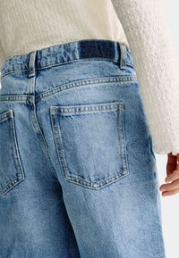 Jeans de mezclilla de un azul claro con un diseño de cintura alta, que cuentan con dos bolsillos traseros y detalles de costura visibles.