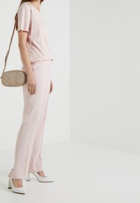 Light pink top with studded lettering, paired with light pink tailored pants. White high heels and a tan quilted crossbody bag complete the look.