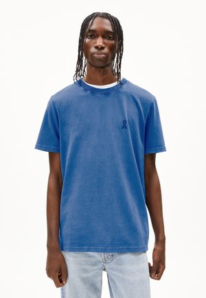 T-shirt en coton bleu avec un col rond, des manches courtes et un petit logo bleu marine sur la poitrine gauche. Porté avec un jean en denim clair.