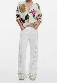 Floral-patterned cardigan in cream with button front, paired with high-waisted white pants featuring accent stitching and side pockets.
