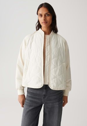 Witte gestikte jas met een staande kraag en rits, met een relaxte pasvorm en lange mouwen, gecombineerd met donkergrijze jeans.