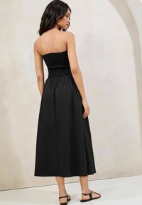 Rochie maxi fără bretele, de culoare neagră, cu un bust smocat, fustă fluidă și lungime până la gleznă. Stilizată cu sandale simple negre.