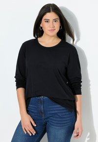 Schwarzes Langarmshirt aus weichem Material, mit rundem Ausschnitt und lockerer Passform, kombiniert mit blauen Denim-Jeans.
