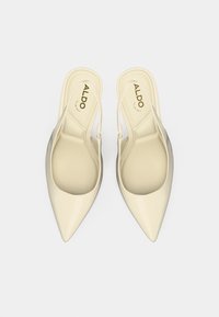 Chaussures beige en cuir verni à enfiler avec un bout pointu et un talon ouvert. Présentent un design élégant et une texture lisse. Logo de la marque visible à l'intérieur.