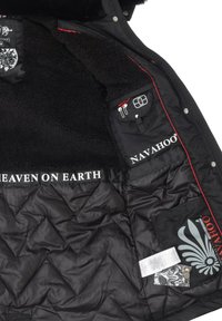 Schwarze gesteppte Jacke mit einem plüschigen, schwarzen Pelzfutter. Verfügt über Innen pockets, rote Akzente und Logo-Details. "HIMMEL AUF ERDEN" wird auffällig angezeigt.