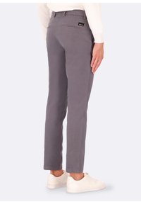 Pantaloni grigi slim fit, realizzati in cotone, dotati di due tasche posteriori e di un'etichetta con marchio. Abbinati a scarpe da ginnastica bianche.