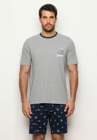 T-shirt di cotone grigia con maniche corte, colletto a costine blu navy e grafica a tema vela sul lato sinistro del petto. Abbinato a pantaloni corti blu navy con stampe nautiche bianche.