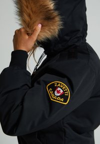 Fekete téli dzseki műszőrme kapucni díszítéssel, vállpattenterekkel "Zavetti Canada" felirattal, és állítható zsinórokkal. Simább textúra.