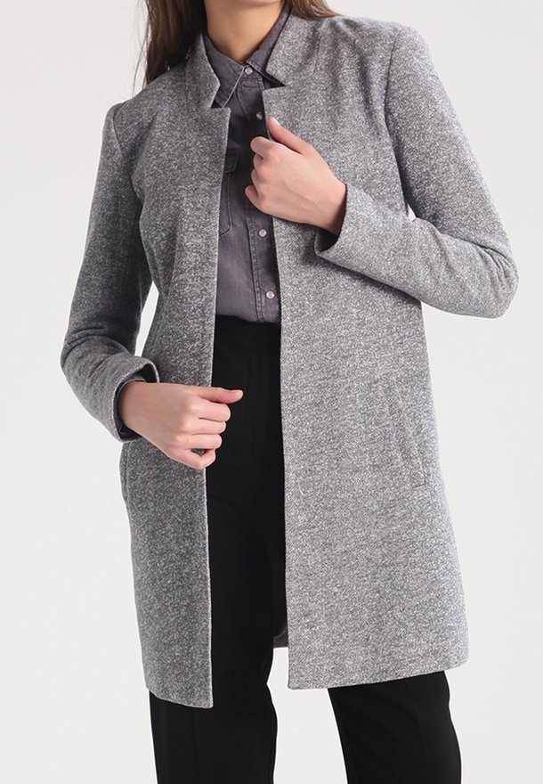 Cappotto grigio con texture, con colletto, maniche lunghe, apertura frontale e tasche laterali. Indossato sopra una camicia con bottoni e pantaloni neri.