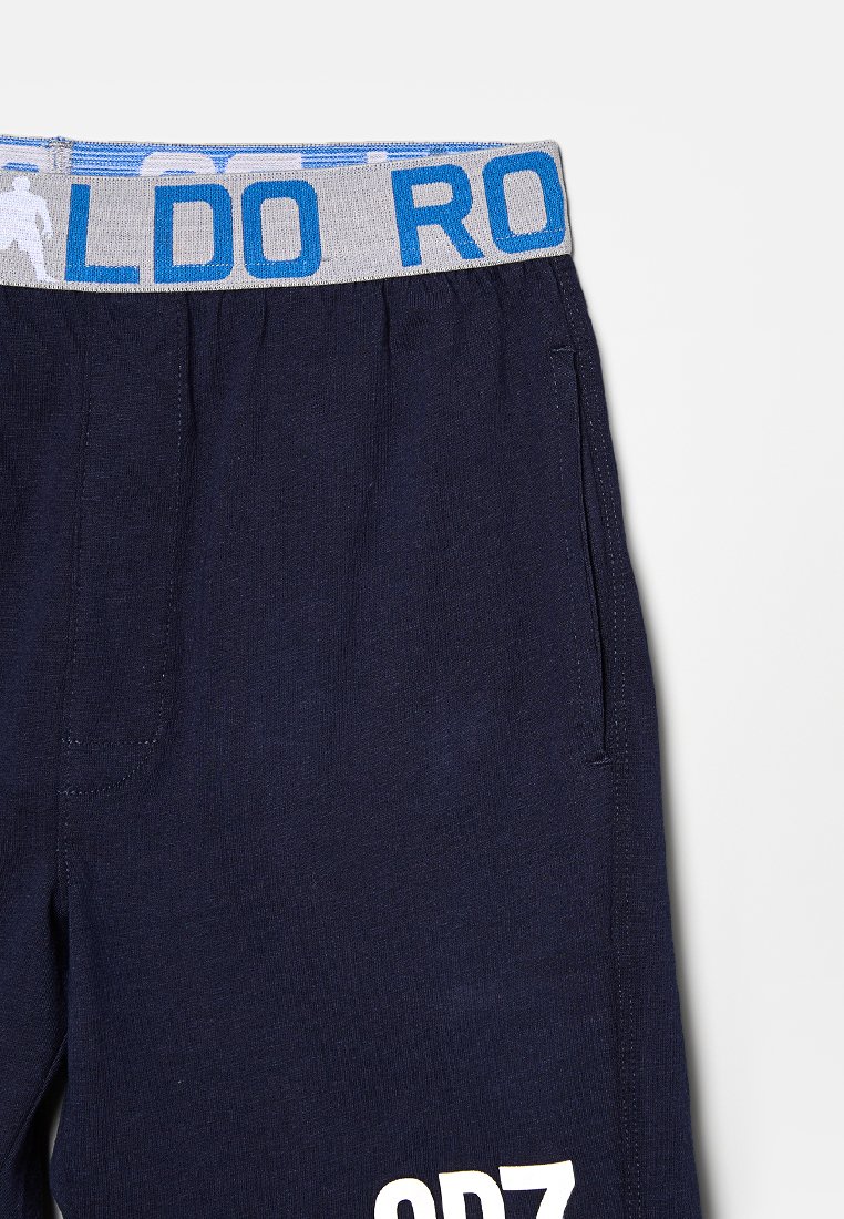 Pantalons de jogging bleu marine avec un waistband élastique gris portant "CR7" en bleu. Texte blanc "ODZ" sur la jambe gauche. Tissu doux et texturé.