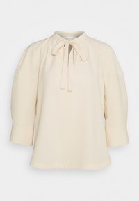 Blusa crema con collo alto, dettaglio a fiocco, maniche a tre quarti e sottili rifiniture cucite sulle maniche e sul corpino.