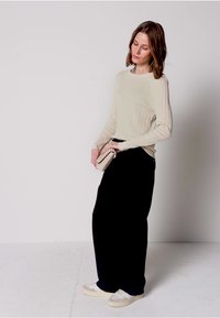 Beige ribstrikket sweater, sort lang nederdel, holder en tekstureret cremefarvet håndtaske, kombineret med hvide sneakers. Simpelt design, bløde teksturer og neutrale farver.