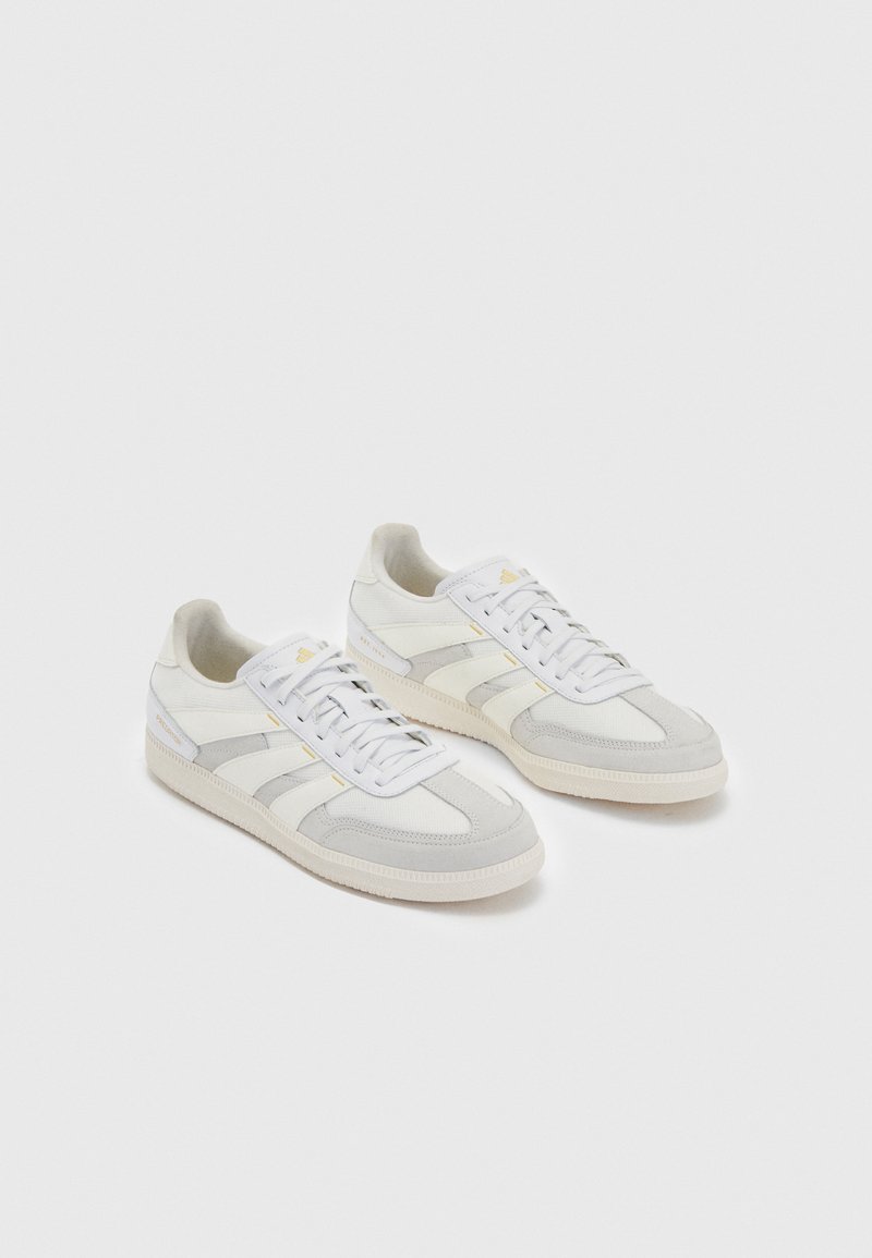 Biele tenisky s svetlo šedými semišovými akcentmi a pruhmi, s textúrovaným textilným zvrškom, plochými šnúrkami a gumovou podrážkou.