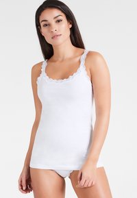 White camisole with delicate lace trim and adjustable straps, made of soft fabric, featuring a fitted design.