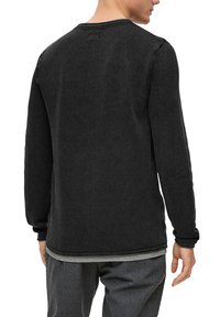 Schwarzer Pullover mit langen Ärmeln aus strukturiertem Strickstoff, Rundhalsausschnitt und gerippten Bündchen. In der Mitte über einem grauen Hemd geschichtet.