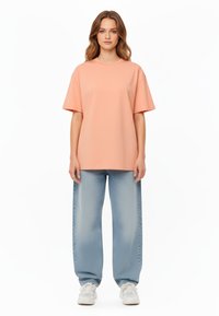 T-shirt oversize pesco con maniche corte, abbinato a jeans baggy blu chiaro e sneakers bianche. Tessuto morbido, design semplice, senza motivi.