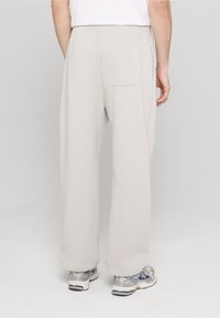 Pantaloni sport gri deschis din material moale, cu o croială lejeră și un buzunar în spate. Purtați cu adidași gri.