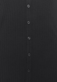 Cardigan noir côtelé avec une rangée de six boutons au centre. Le tissu a une texture lisse avec des lignes verticales.