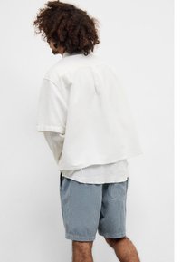 Overdimensjonert lys beige skjorte med rå kant, lagd over en tettsittende hvit langermet genser. Sammen med midjelange blå kordfløyelsshorts.