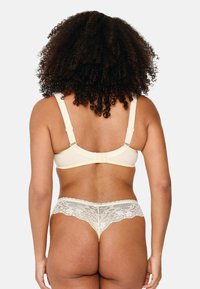Set di biancheria intima e reggiseno rifinito in pizzo beige. Il reggiseno ha spalline regolabili e una texture liscia. Il pizzo presenta un motivo floreale che arricchisce il design.