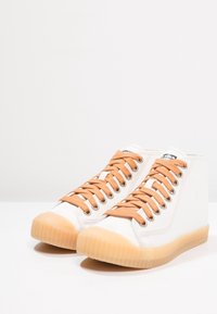 Białe wysokie trampki z jasnobrązowymi sznurówkami i podeszwami z gumy. Teksturalny materiał wierzchni z metalowymi oczkami i naszywką z logo na języku.