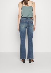 Tummansininen flare-mallinen farkut, joissa on korkea vyötärö. Farkuissa on kaksi takataskua ja pieni kolmion muotoinen logopatch vyötärömuodostelmassa.