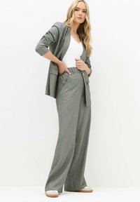 Grijs gestreepte blazer met een bijpassende broek met wijde pijpen. Beide kledingstukken hebben een ontspannen fit en zijn gemaakt van een gladde stof. Witte top eronder.