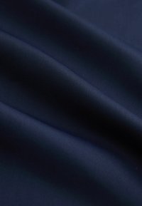 Hladká tmavě modrá látka s jemnou texturou a měkkými záhyby vytvářejícími jemné stíny a zvýraznění.