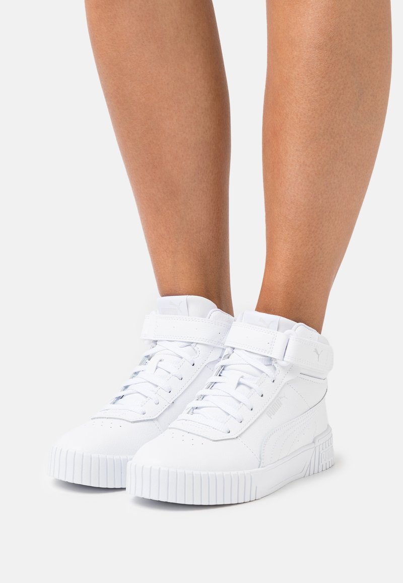White high-top sneakers made of synthetic material with a rippled rubber sole, featuring a Velcro strap and lace-up front.