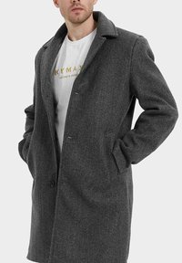 Manteau en laine gris avec un col à revers, fermeture à un bouton et deux poches latérales. Présente un tissu texturé et une coupe décontractée.