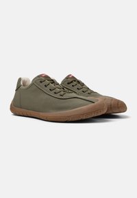 Green canvas sneakers with a rubber sole, lace-up design, and contrasting tan outsole. Features red logo on the tongue.