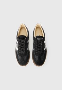 Scarpe da atletica nere con accenti in feltro grigio, dettagli in suede, strisce laterali bianche, lacci neri e una suola in gomma marrone.