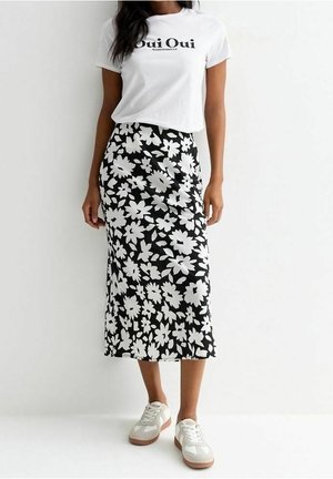 Femme portant un t-shirt blanc « Oui Oui », une jupe midi noire à motif floral blanc, et des baskets blanches avec des semelles marron clair.