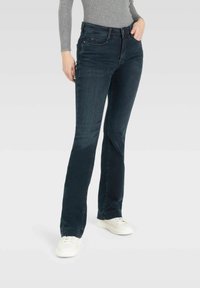 Dunkelblaue Schlagjeans mit Fünf-Taschen-Design, aus Denim gefertigt, mit einer mittelhohen Taille und dezenten Stickdetails. Weiße Sneakers werden getragen.