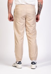 Joggers de nylon beige con cintura y puños elásticos, que cuentan con bolsillos laterales y una textura suave. Combinados con zapatillas blancas.