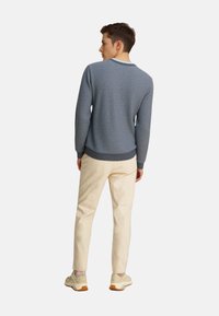 Gebreide blauwe trui met een gestructureerd patroon, geribbelde manchetten en zoom, gecombineerd met crèmekleurige broek en lichte sneakers.