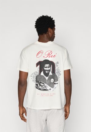 Camiseta de algodón blanca con un estampado gráfico en negro y rojo de un jugador de fútbol con el número "10" y el texto "O Rei" en la parte de atrás.