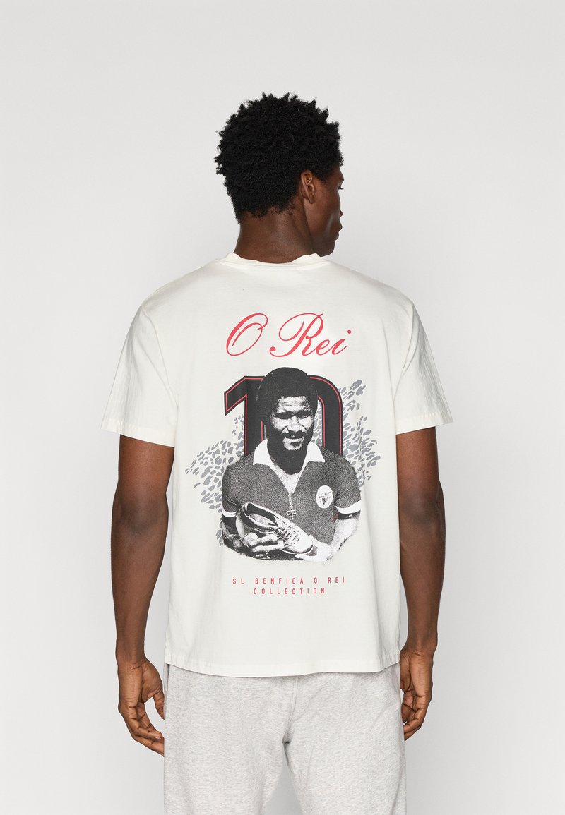 Λευκό βαμβακερό T-shirt με μαύρη και κόκκινη γραφική εκτύπωση ενός ποδοσφαιριστή με τον αριθμό "10" και το κείμενο "O Rei" στην πλάτη.