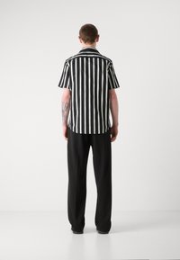 Chemise à rayures verticales noires et blanches à manches courtes, associée à un pantalon noir. Dispose d'une coupe décontractée et d'un col pointu.