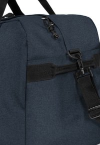 Bolsa de lona azul oscuro hecha de tejido texturizado, con correas de nailon negro, clips y un cierre de cordón en la parte superior.