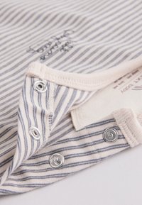 Close-up of beige and gray striped fabric with metal snap buttons and visible stitching on soft clothing item.